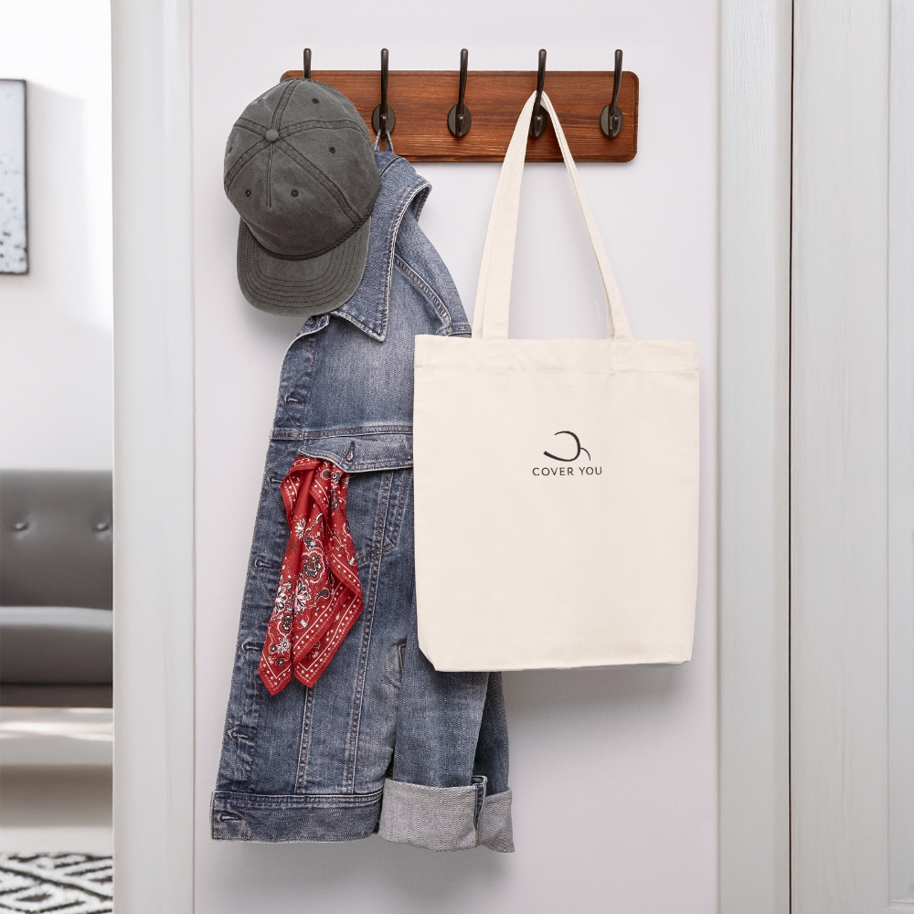 Tote bag COVER YOU blanc cassé suspendu à une patère près d'une veste en jean
