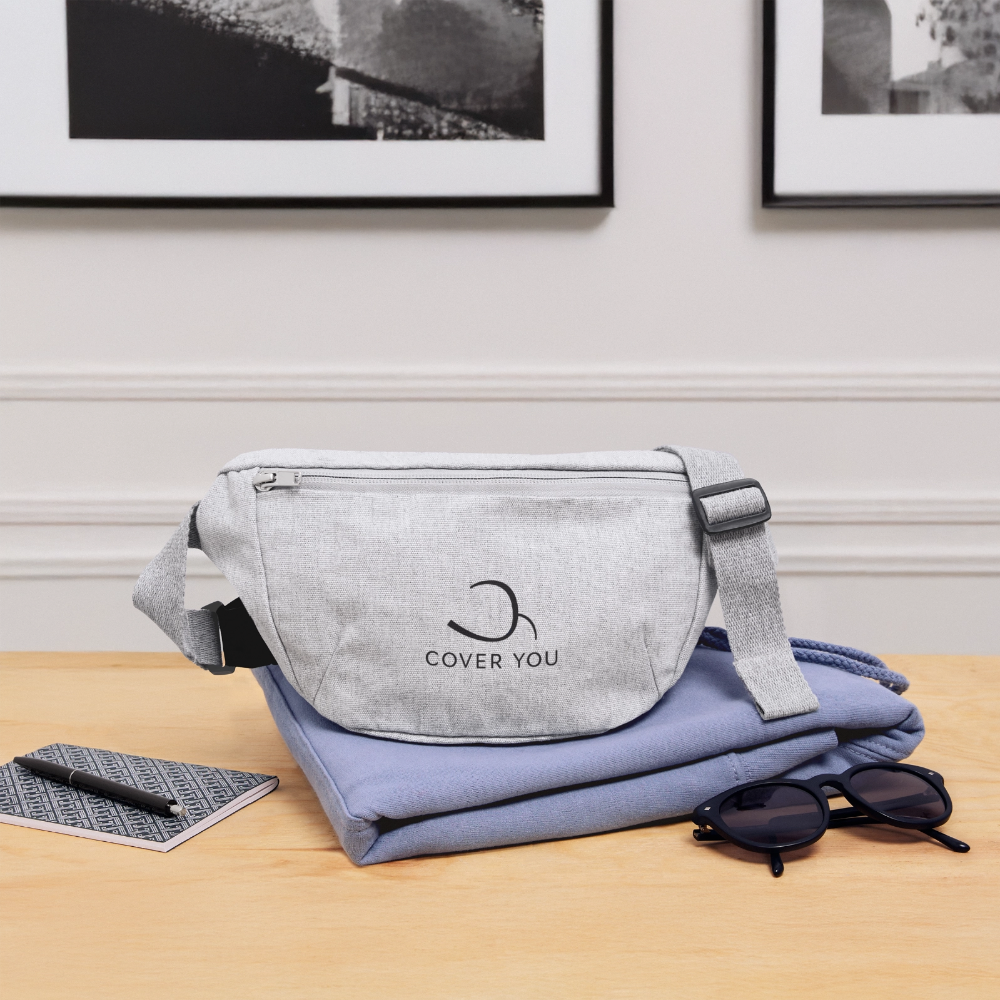 Sac banane COVER YOU gris chiné posé sur une chemise pliée, près d'un carnet et de lunettes de soleil