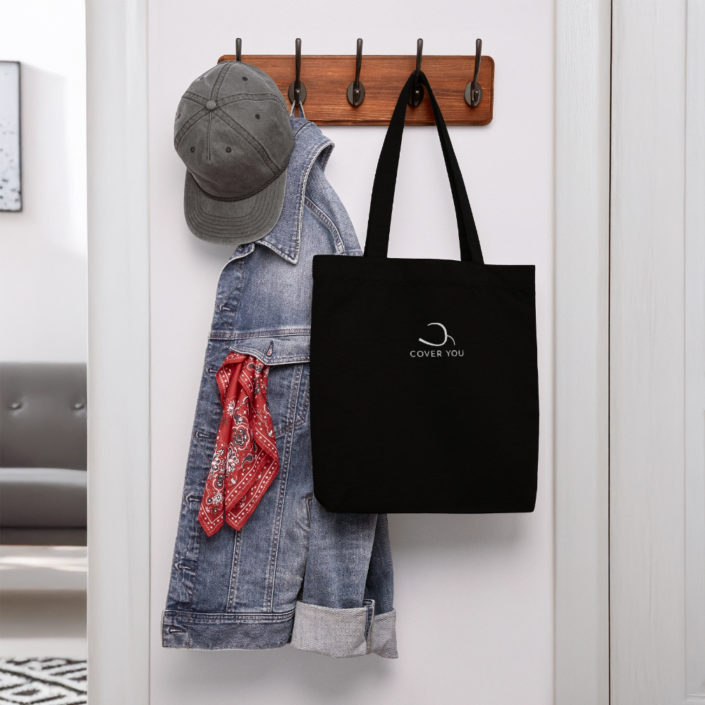 Tote bag COVER YOU noir suspendu à une patère près d'une veste en jean